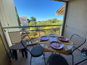 Un balcon avec une table dressée pour quatre personnes, donnant sur un jardin et des immeubles.