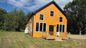 A two-story wooden cabin with a porch, surrounded by a grassy field and trees. - Unwind at The Highland Sunset—a comfortable three bedroom retreat. (Princeton)