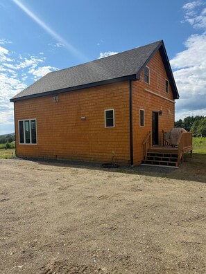 Ein zweistöckiges Holzhaus mit einer Laube und einer Schotterzufahrt.