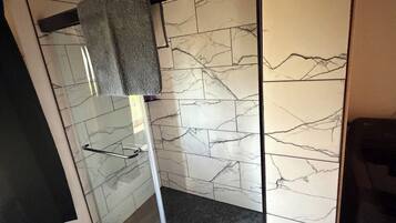 Um banheiro moderno com box de vidro, paredes de mármore e teto de madeira.