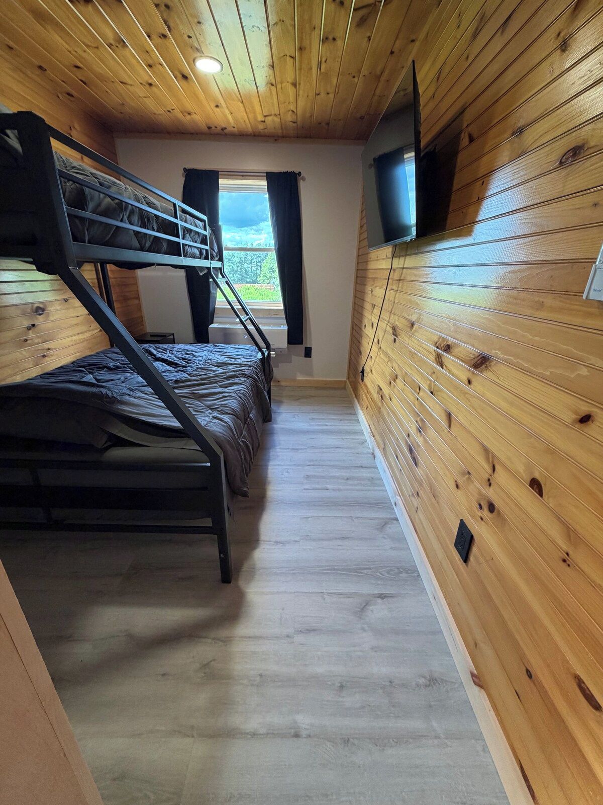 A bunk bed room with wooden walls and a window.
