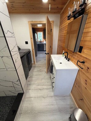 Un baño moderno con un lavamanos blanco, paneles de madera y un salpicadero de mármol.