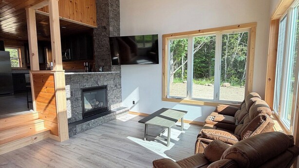 A spacious living area with a stone fireplace, wooden ceiling, and a large window providing a view of the outdoors. - Unwind at The Highland Sunset—a comfortable three bedroom retreat. (Princeton)