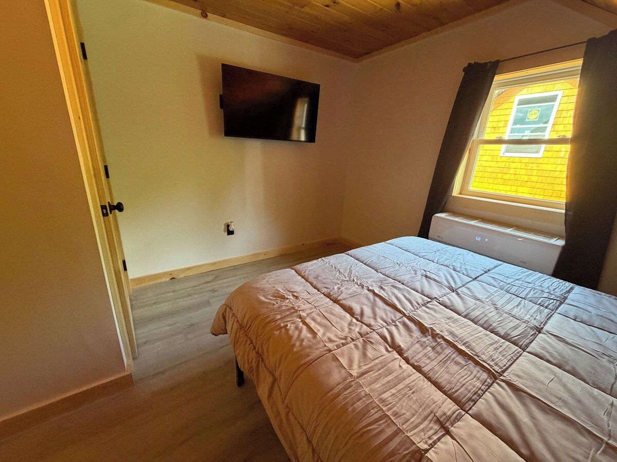 Une chambre à coucher avec un lit, un téléviseur fixé au mur, une fenêtre avec des rideaux et un radiateur.