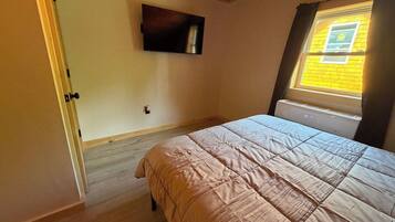 Une chambre à coucher avec un lit, un téléviseur fixé au mur, une fenêtre avec des rideaux et un radiateur.