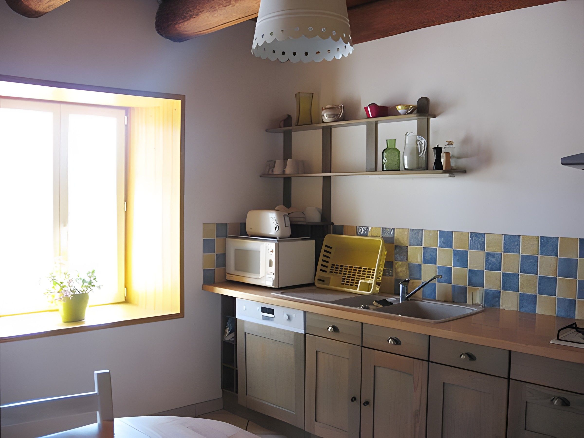 Een keuken met een raam, een magnetron, een gele mand en planken met diverse keukengerei.