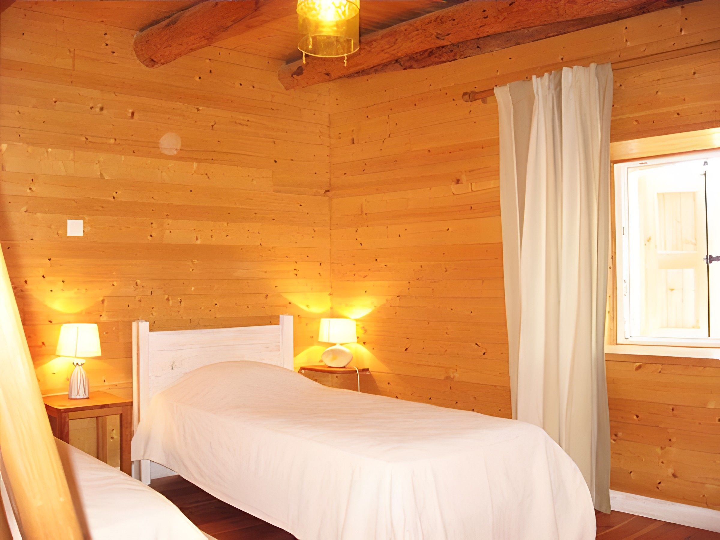 Een houten kamer met twee bedden, een raam met gordijnen en wandlampen.