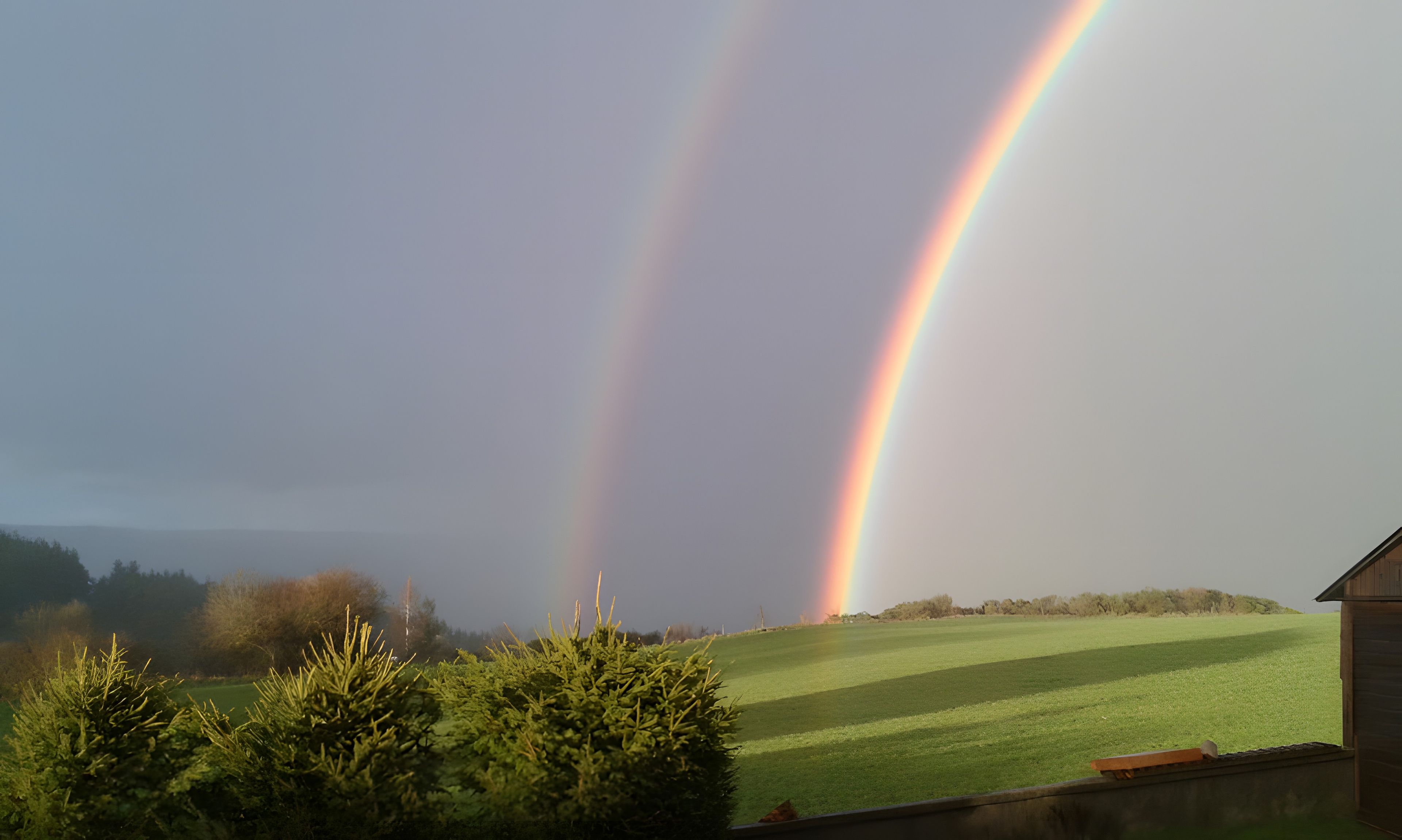 Een landschap met een regenboog, een grasveld en een gebouw op de voorgrond.