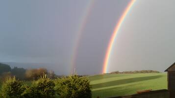 Een landschap met een regenboog, een grasveld en een gebouw op de voorgrond.