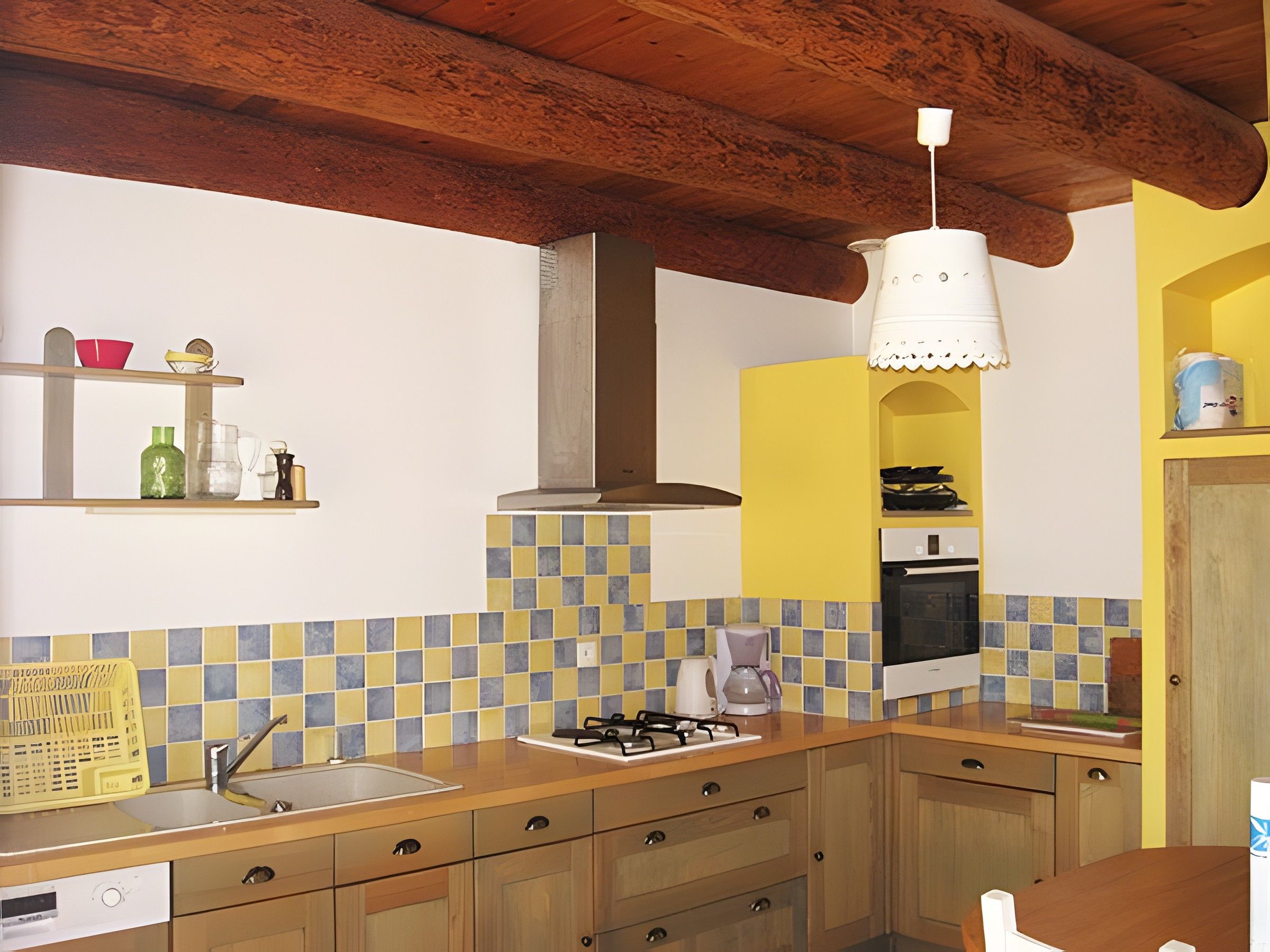 Een keuken met een betegelde spatwand, houten kastjes, een spoelbak, een fornuis en een hanglamp.