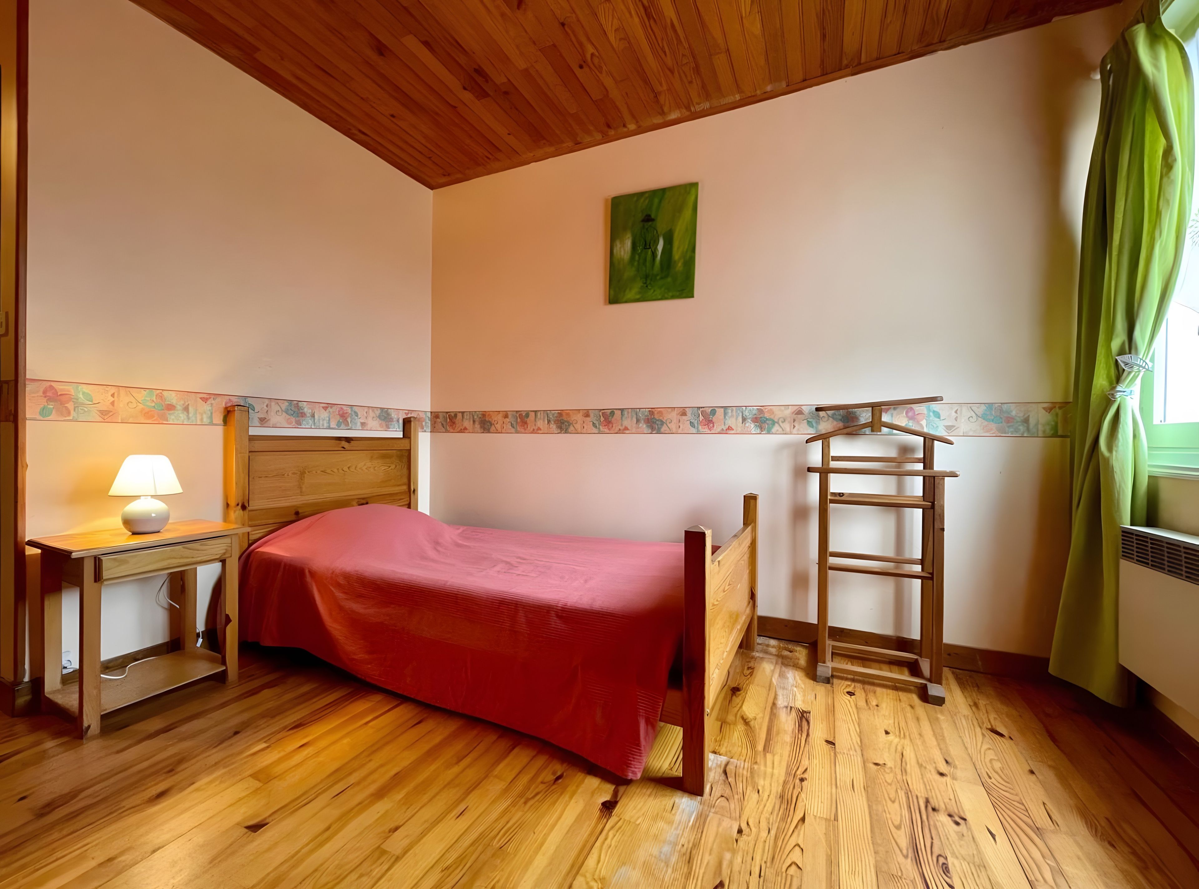 Ein Zimmer mit einem hölzernen Bett, einem Nachttisch mit Lampe, einer Leiter und einem Fenster mit Vorhängen.