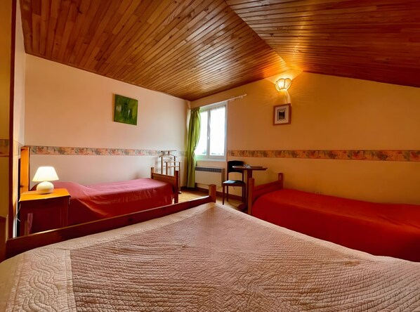 A room with two beds, a desk, a chair, a lamp, and a window with curtains.