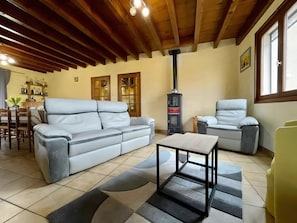 Una sala de estar con un sofá, sillones, una mesa, una chimenea y un comedor con sillas y una estantería llena de botellas.