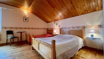 A bedroom with a wooden ceiling, a single bed, a chair, a small table, and a nightstand with a lamp.