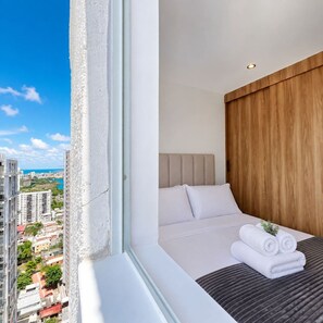 A hotel room with a large window, a bed with white linens, a wooden headboard, and a view of the cityscape. - Coconut Palm | City Views, Marbella Beach & Pool (Cartagena)