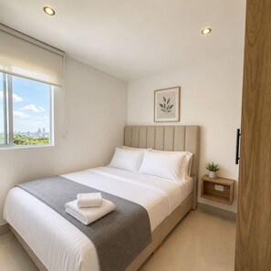 A modern bedroom with a large bed, a bedside table with a plant, and a window with a city view. - Coconut Palm | City Views, Marbella Beach & Pool (Cartagena)