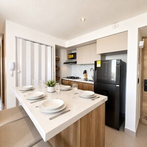 A modern kitchen with a central island, a black refrigerator, and a built-in stove. - Coconut Palm | City Views, Marbella Beach & Pool (Cartagena)