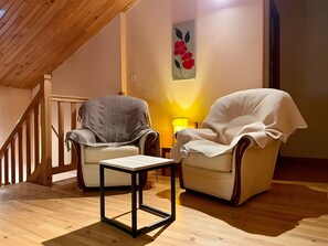 A cozy room with a wooden ceiling, two armchairs, a small table, and a lamp.