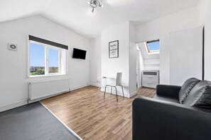 A modern, well-lit room with a wooden floor, a black leather sofa, a small table, and a chair. - Spacious studio near Leeds City Centre - Room 7 (Leeds)