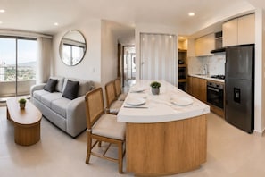 A modern kitchen with a central island, dining area with a sofa, and a view through a window. - Royal Palm | Old Town Views, Marbella Beach & Pool (Cartagena)