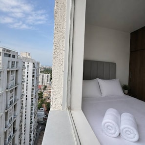 A hotel room with a bed, pillows, and a view of the cityscape. - Royal Palm | Old Town Views, Marbella Beach & Pool (Cartagena)