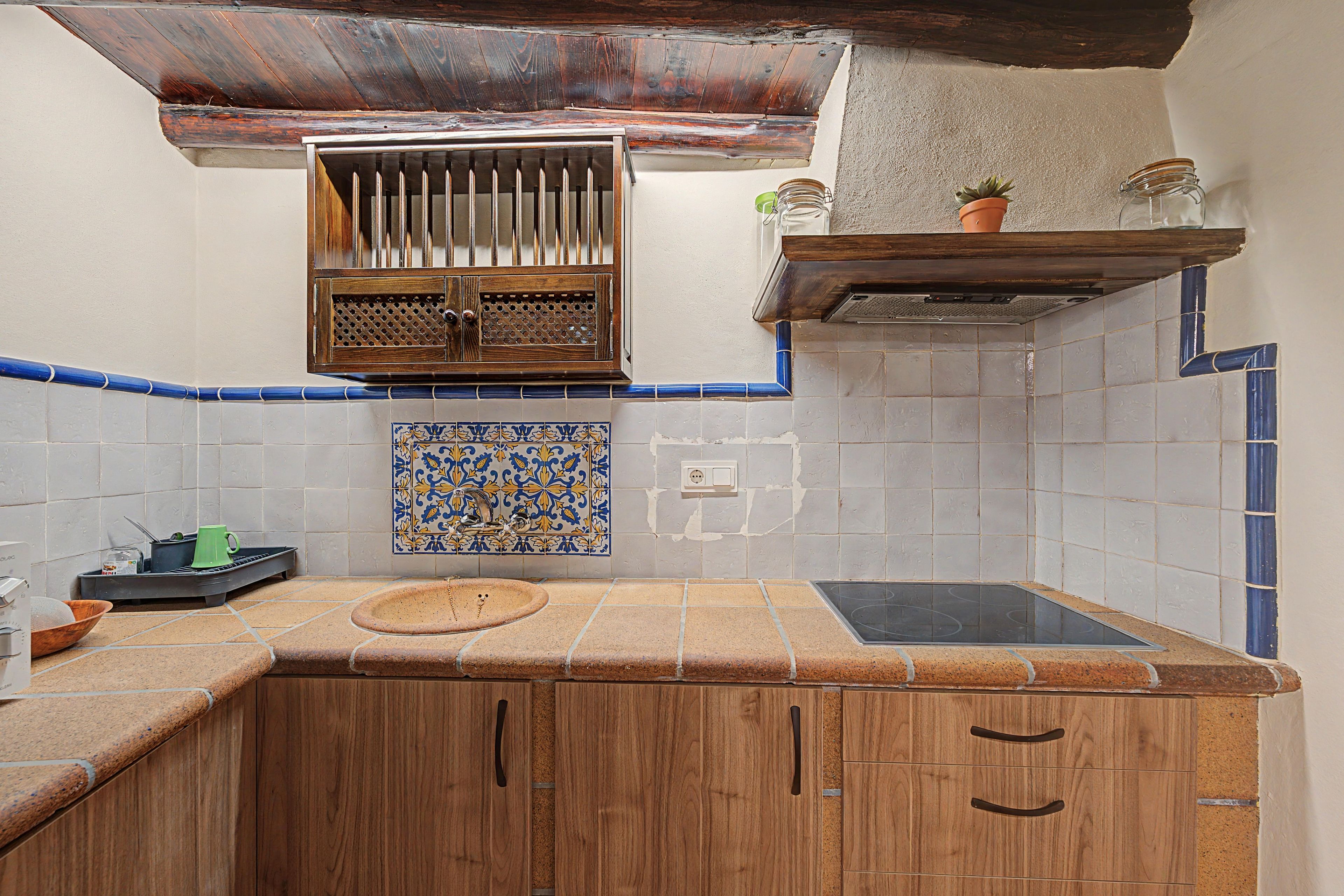 Une cuisine avec des meubles de rangement en bois, une cuisinière encastrée et un pare-feu décoré de carreaux bleus et blancs.