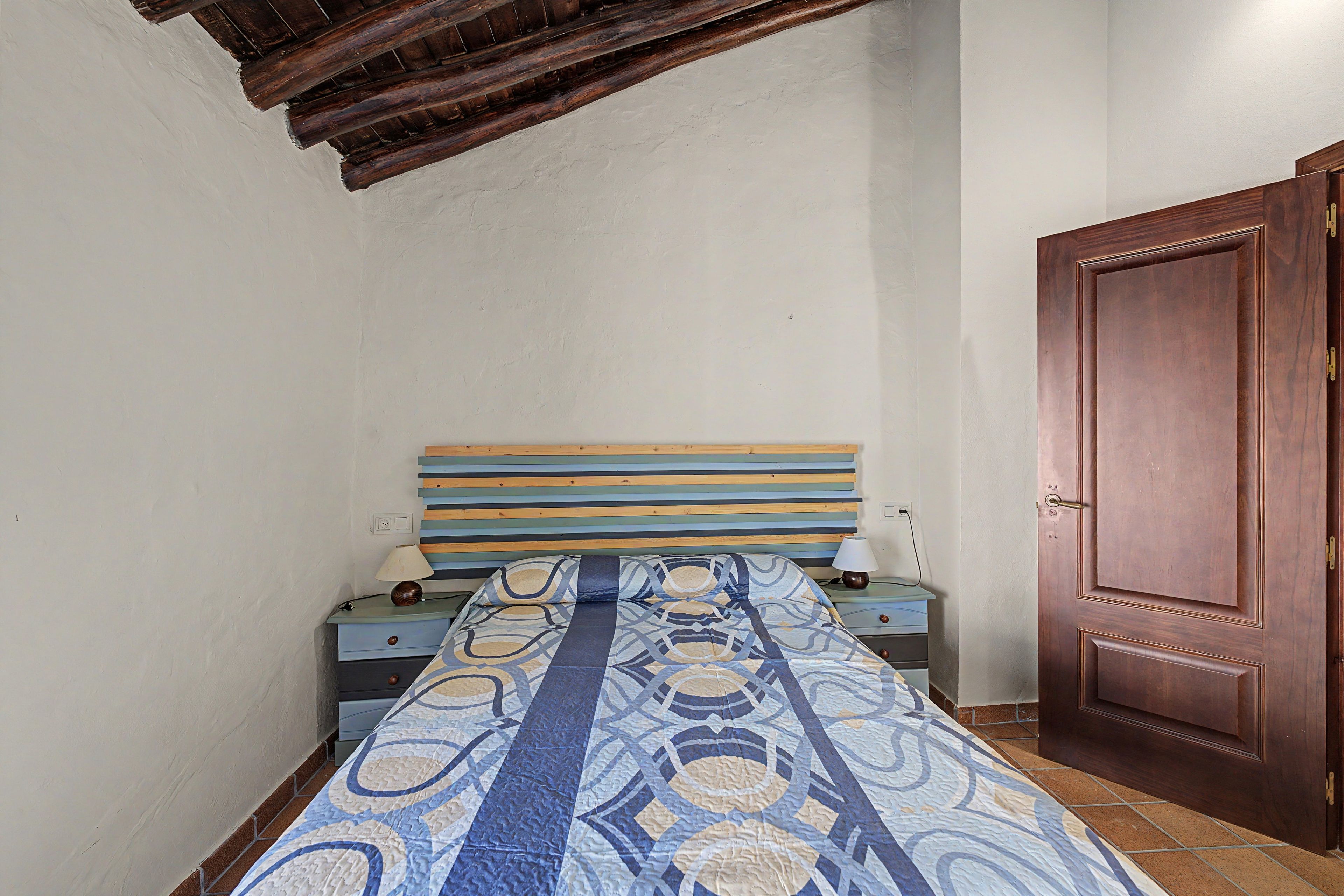 Una habitación pequeña y estrecha con una cama individual, una puerta de madera y un techo inclinado.