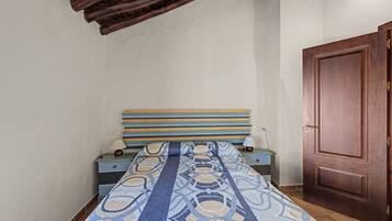 Una habitación pequeña y estrecha con una cama individual, una puerta de madera y un techo inclinado.