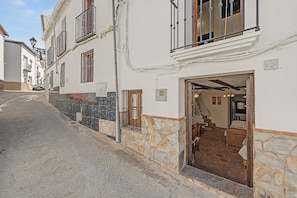 Vista de una calle que muestra un edificio con fachada de piedra, puerta de madera y una escalera que lleva a un piso superior.