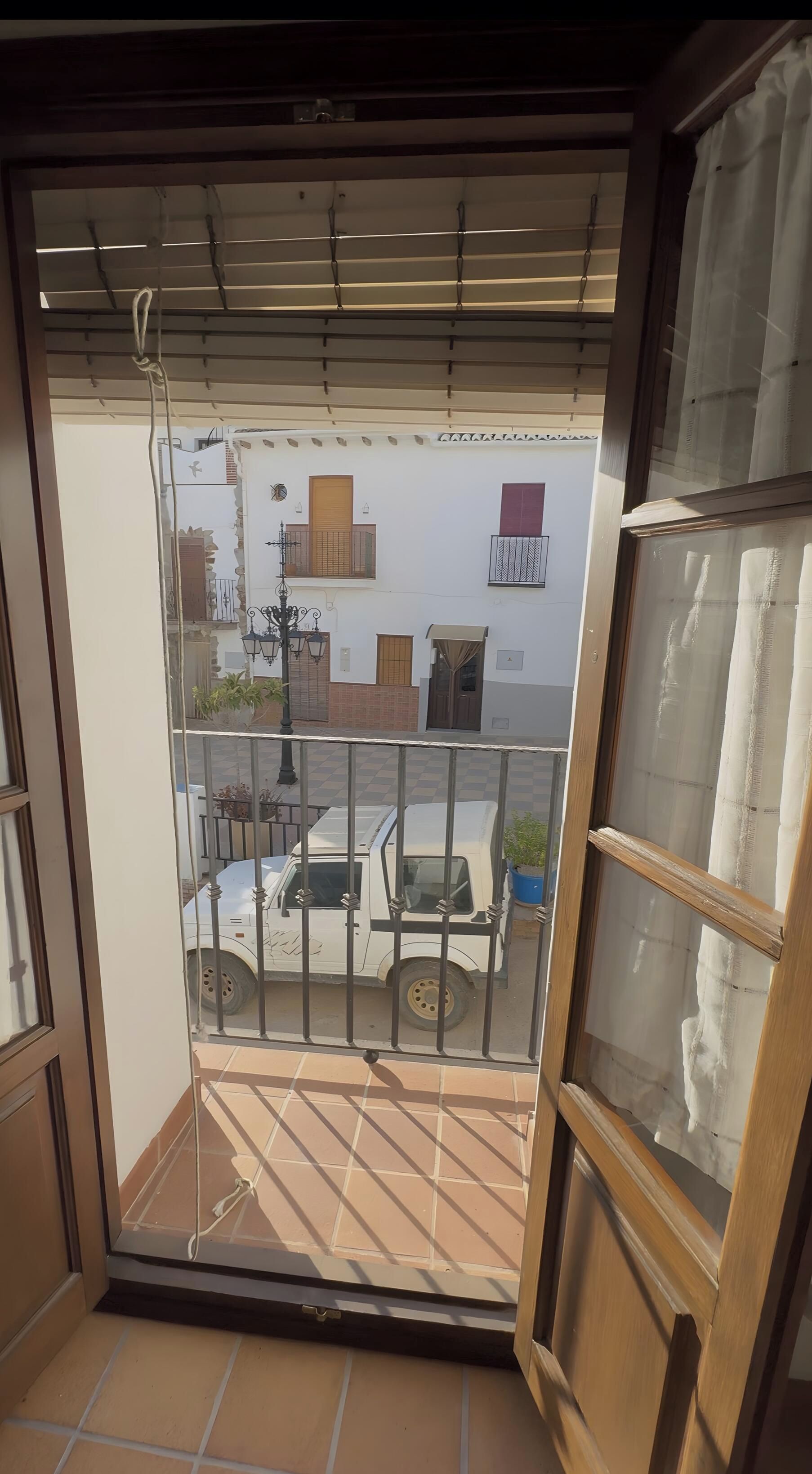 Un balcon donnant sur une rue, un fourgon blanc garé et une rambarde en métal.