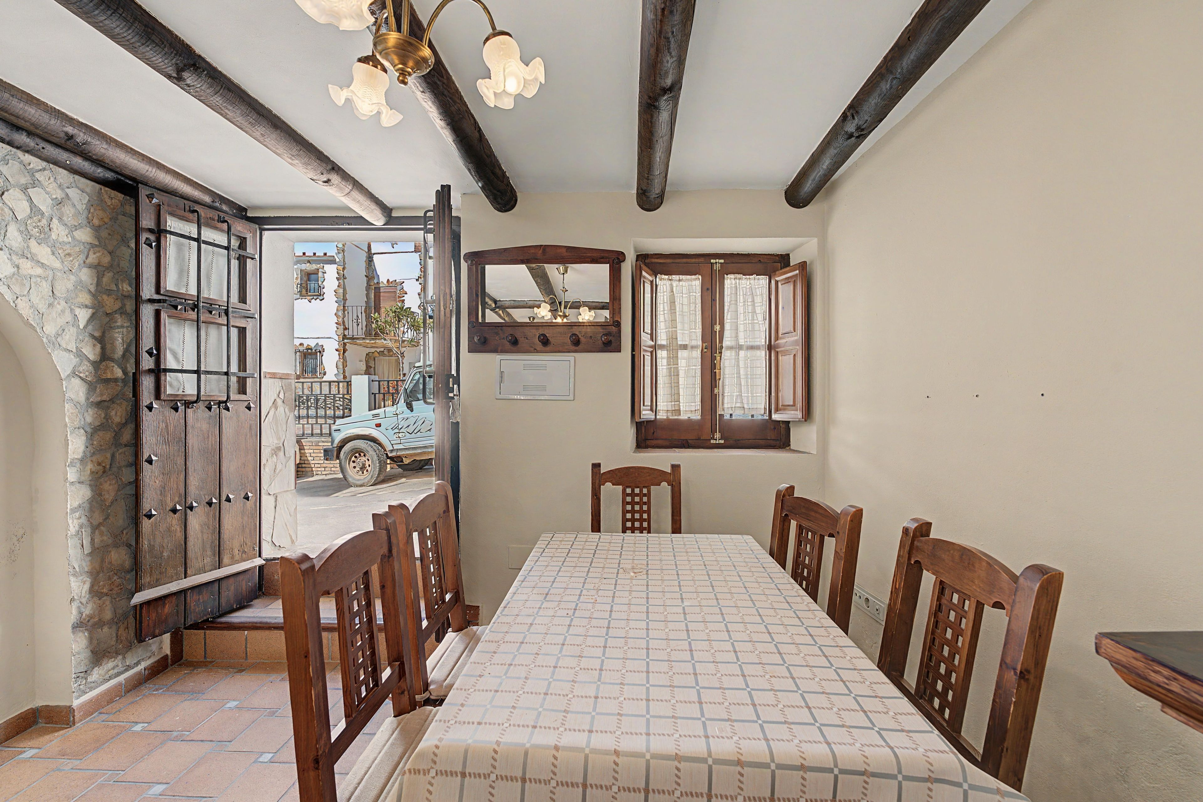 A dining room with a table set for four, wooden chairs, a chandelier, and a stone wall.