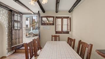 A dining room with a table set for four, wooden chairs, a chandelier, and a stone wall.