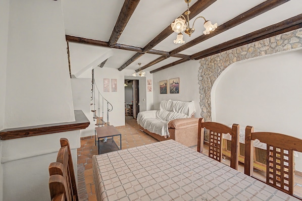 Una habitación con techo de madera, una cama, una mesa y una escalera que conduce a otra habitación.