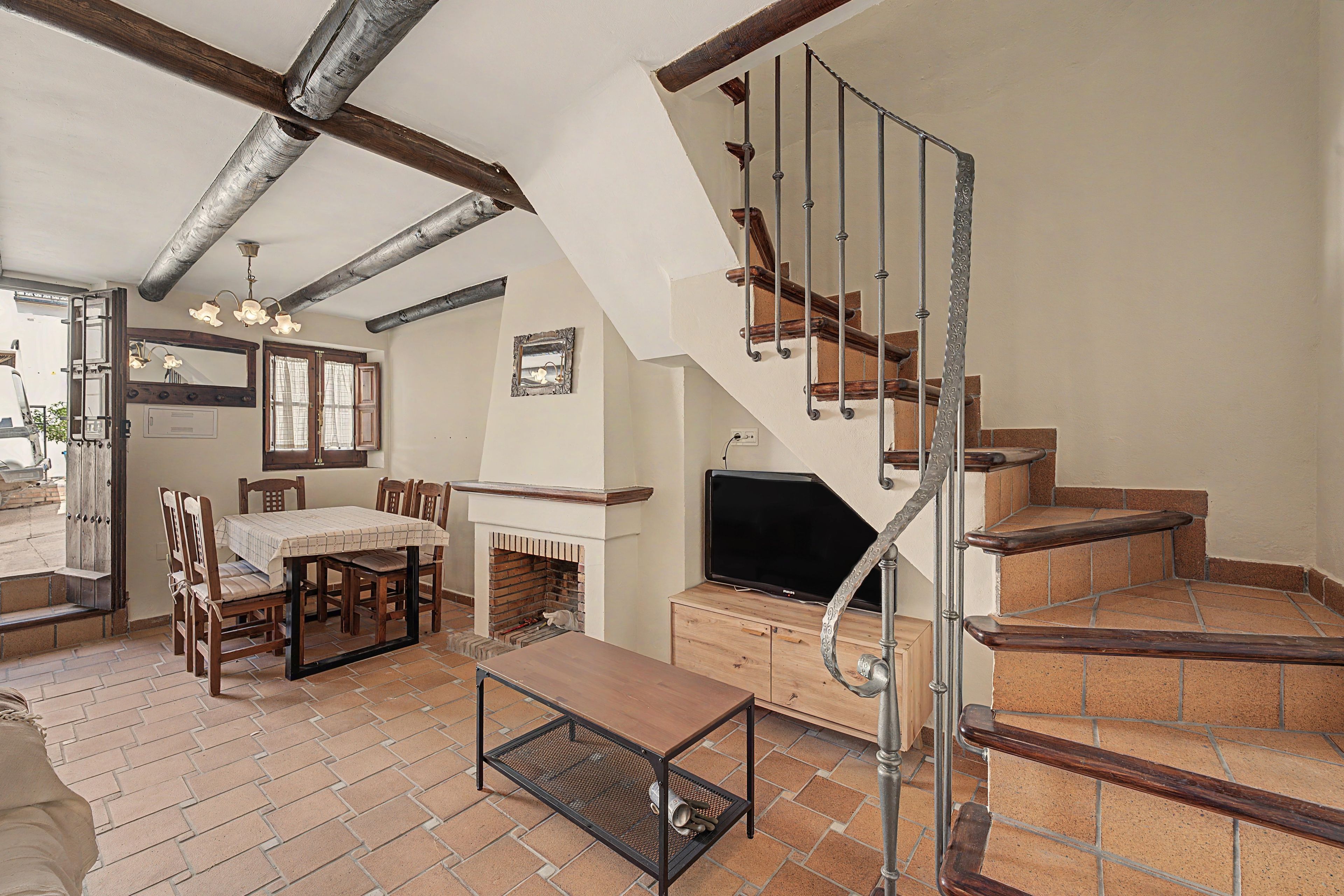 A spacious living area with a fireplace, a dining set, and a staircase with a metal railing.