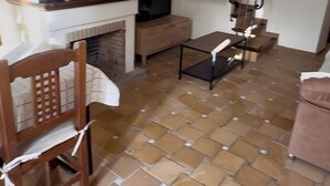 Een kamer met een betegelde vloer, een houten stoel, een tafeltje, een televisie en een open haard.