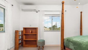 Quarto com cama de dossel, estante de madeira, um banquinho pequeno e janela com persianas.