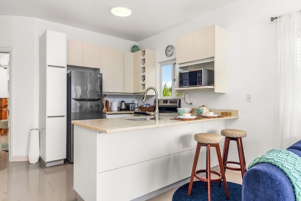 Una cocina moderna con refrigerador, microondas y estufa integrados. Hay dos taburetes y una ventana con vistas.