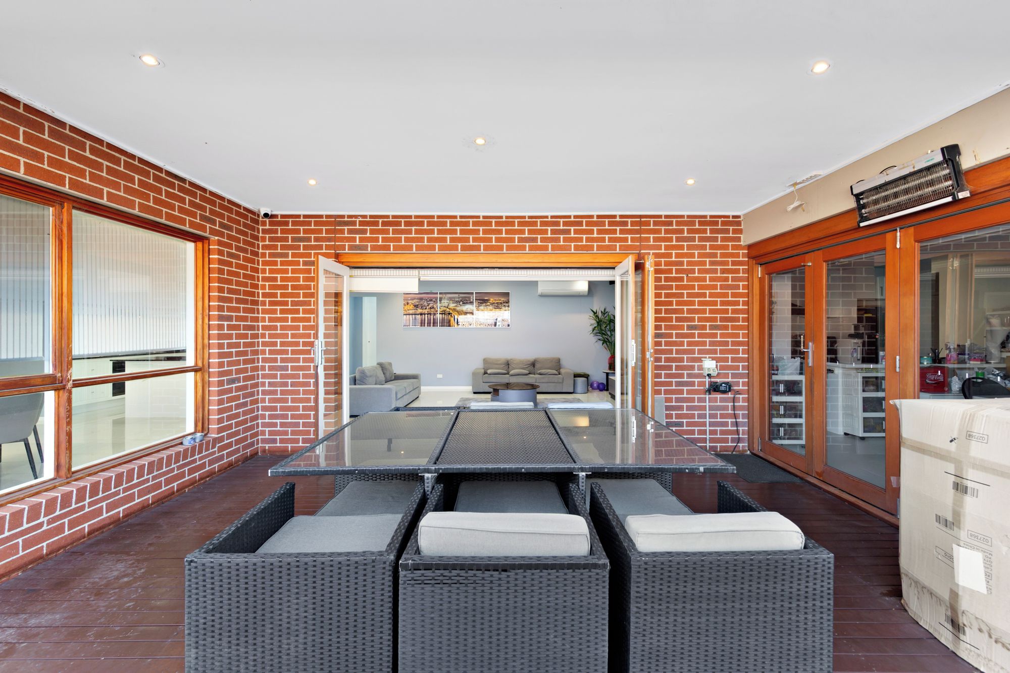 Un patio moderno al aire libre con una mesa de vidrio rodeada de sillas de mimbre, un muro de ladrillo y vistas a una sala de estar.