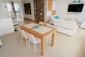 Een moderne woonkamer met een eettafel, witte stoelen, een bank en een wandgemonteerde flatscreen-tv.
