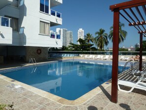 A swimming pool with lounge chairs, a lifebuoy, and a view of tall buildings and palm trees. - Penthouse over the Bay – Sunrise & Ships (Cartagena de Indias)