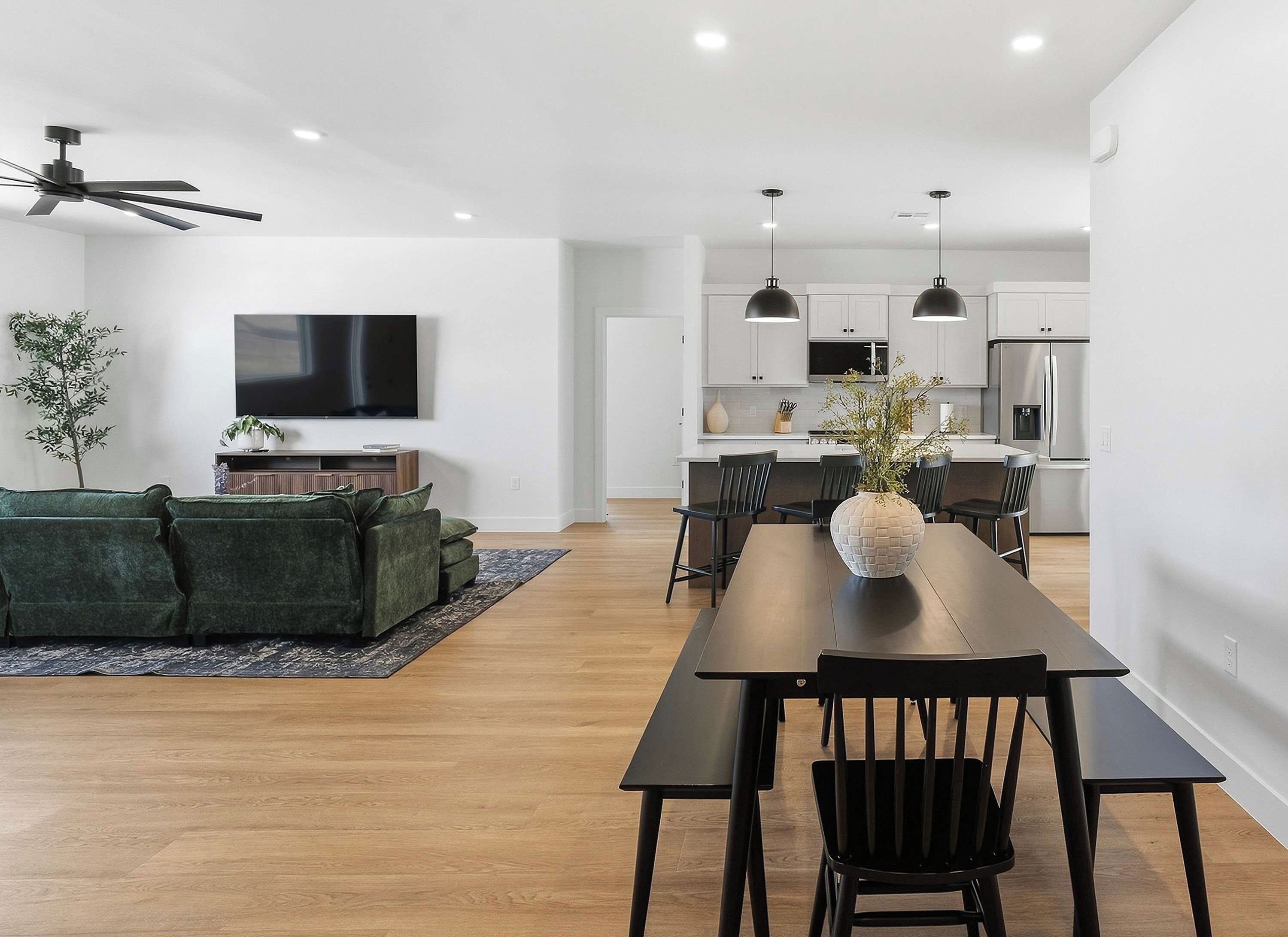 Una sala de estar moderna con un sofá, una mesa de comedor con sillas, un televisor y una cocina con armarios y electrodomésticos.