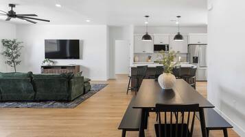 Una sala de estar moderna con un sofá, una mesa de comedor con sillas, un televisor y una cocina con armarios y electrodomésticos.