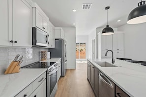 A modern kitchen with white cabinetry, stainless steel appliances, and a large window. - The Basecamp - 4BR Sleeps 14, Modern, Firepit (Page)