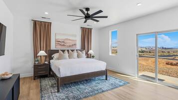 A bedroom with a bed, nightstands, a ceiling fan, a large window with a view, and a painting on the wall.