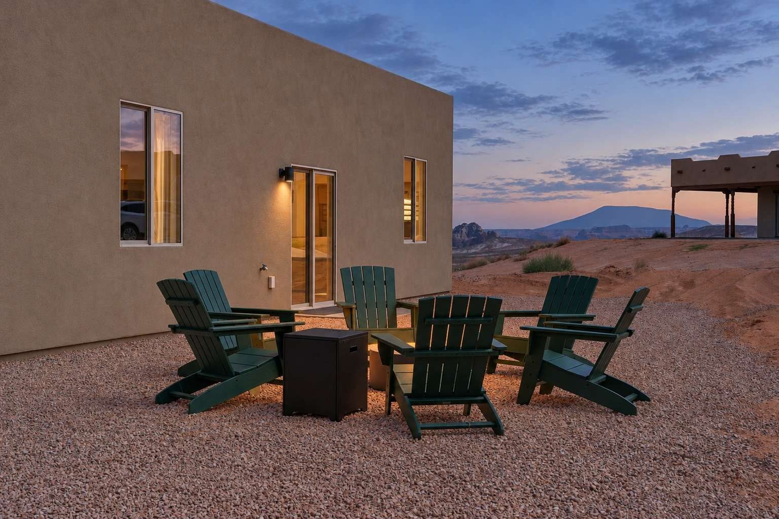 Un bâtiment moderne doté d’une terrasse en gravier, d’un espace extérieur aménagé avec des fauteuils Adirondack et offrant une vue sur une chaîne de montagnes.