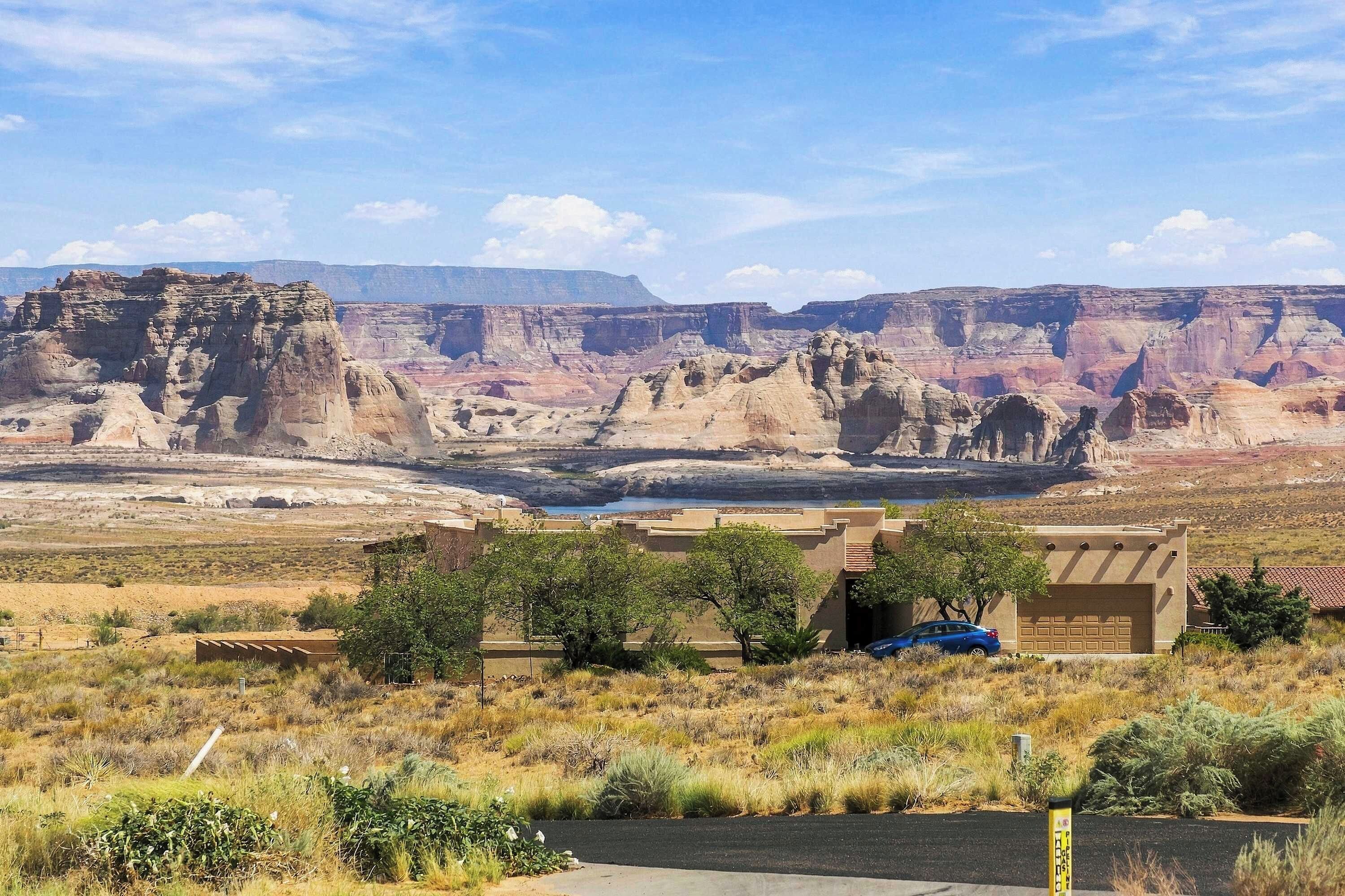 A building with a flat roof and a garage door, surrounded by dry grass and shrubs, with a canyon in the background.