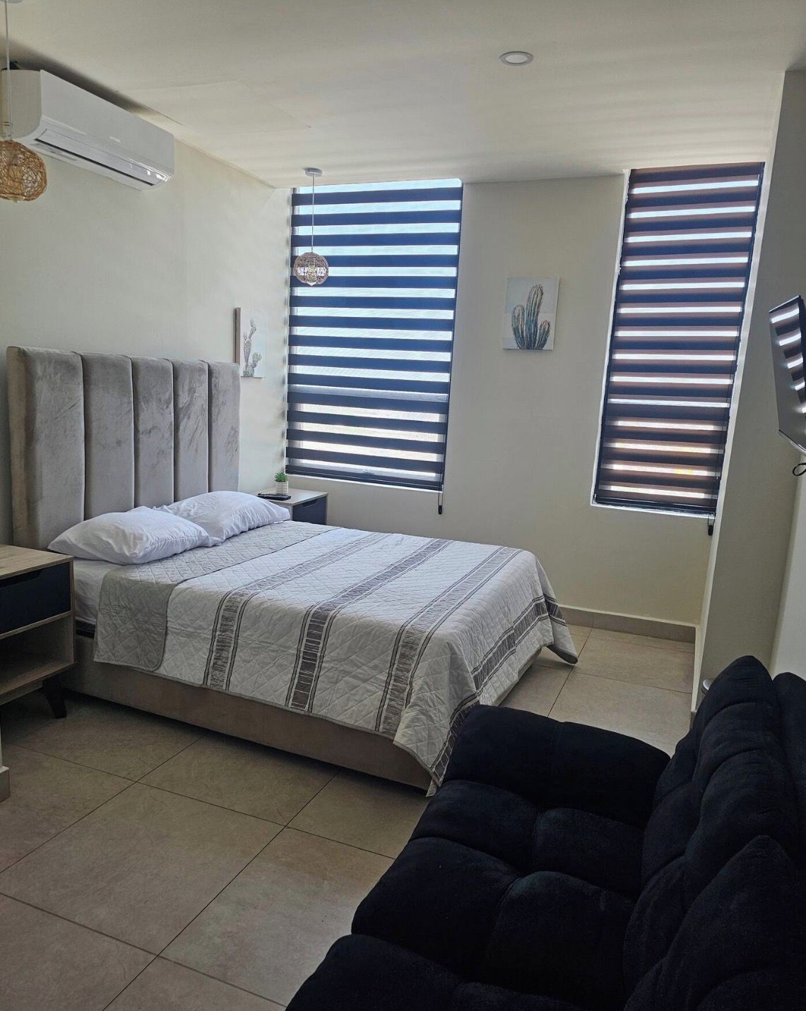 A bedroom with a bed, a nightstand, a dresser, and a window with blinds.