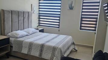 A bedroom with a bed, a nightstand, a dresser, and a window with blinds.