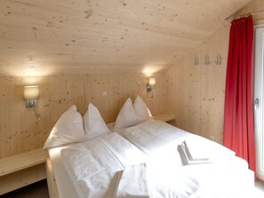 A wooden room with a bed, two wall-mounted lamps, and a red curtain. - One-bedroom Cabin (Sankt Georgen am Kreischberg)