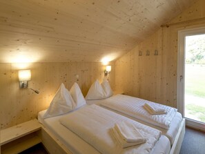 A wooden room with two beds, each with pillows and folded towels. There are wall-mounted lamps and a door leading outside. - One-bedroom Cabin (Sankt Georgen am Kreischberg)